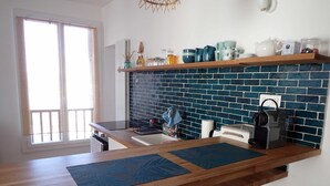 A kitchen with a wooden countertop, two stools, a blue backsplash, and various kitchen items on the shelves.