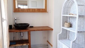 A bathroom with a wooden vanity, a large mirror, a white metal shelf unit, and a black trash bin.