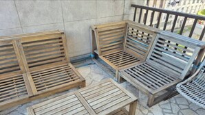 Outdoor wooden furniture including benches and a table, arranged on a stone-tiled patio.