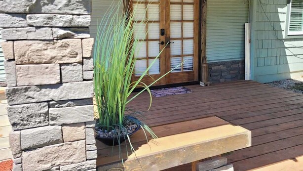 A wooden deck with a stone wall, a wooden door with glass panels, and a potted plant. - 2BR Cabin • 5 Min to Autzen • Park Access • Pet Friendly (Springfield)
