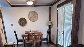 A dining area with a wooden table and chairs, a black leather sofa, and a patterned rug. - 2BR Cabin • 5 Min to Autzen • Park Access • Pet Friendly (Springfield)