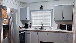 A compact kitchen with a refrigerator, oven, microwave, and a window with blinds. - 2BR Cabin • 5 Min to Autzen • Park Access • Pet Friendly (Springfield)
