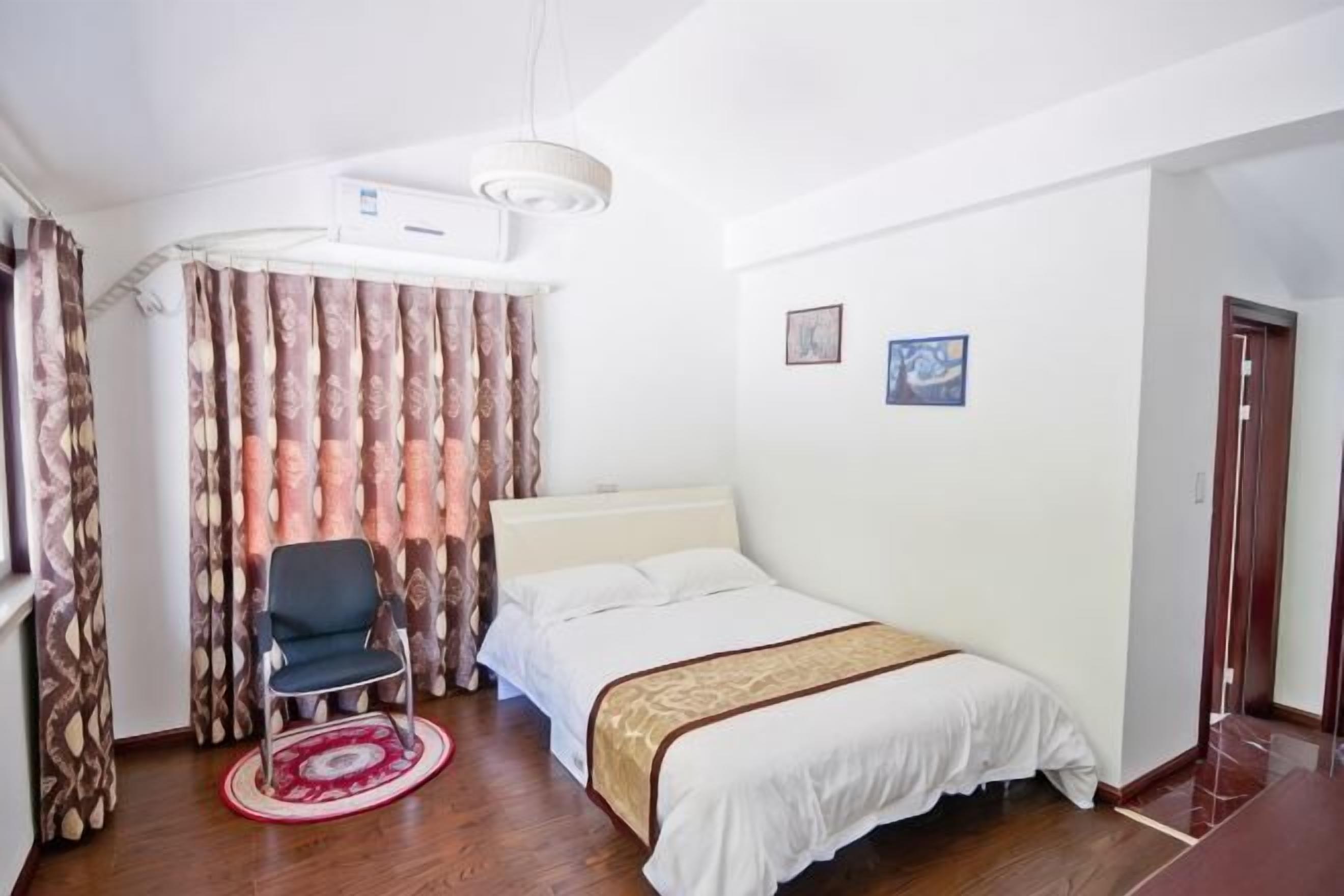 Quarto de hotel com cama, poltrona, escrivaninha e janela com cortinas.