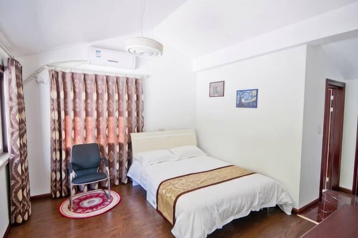 A hotel room with a bed, a chair, a desk, and a window with curtains.