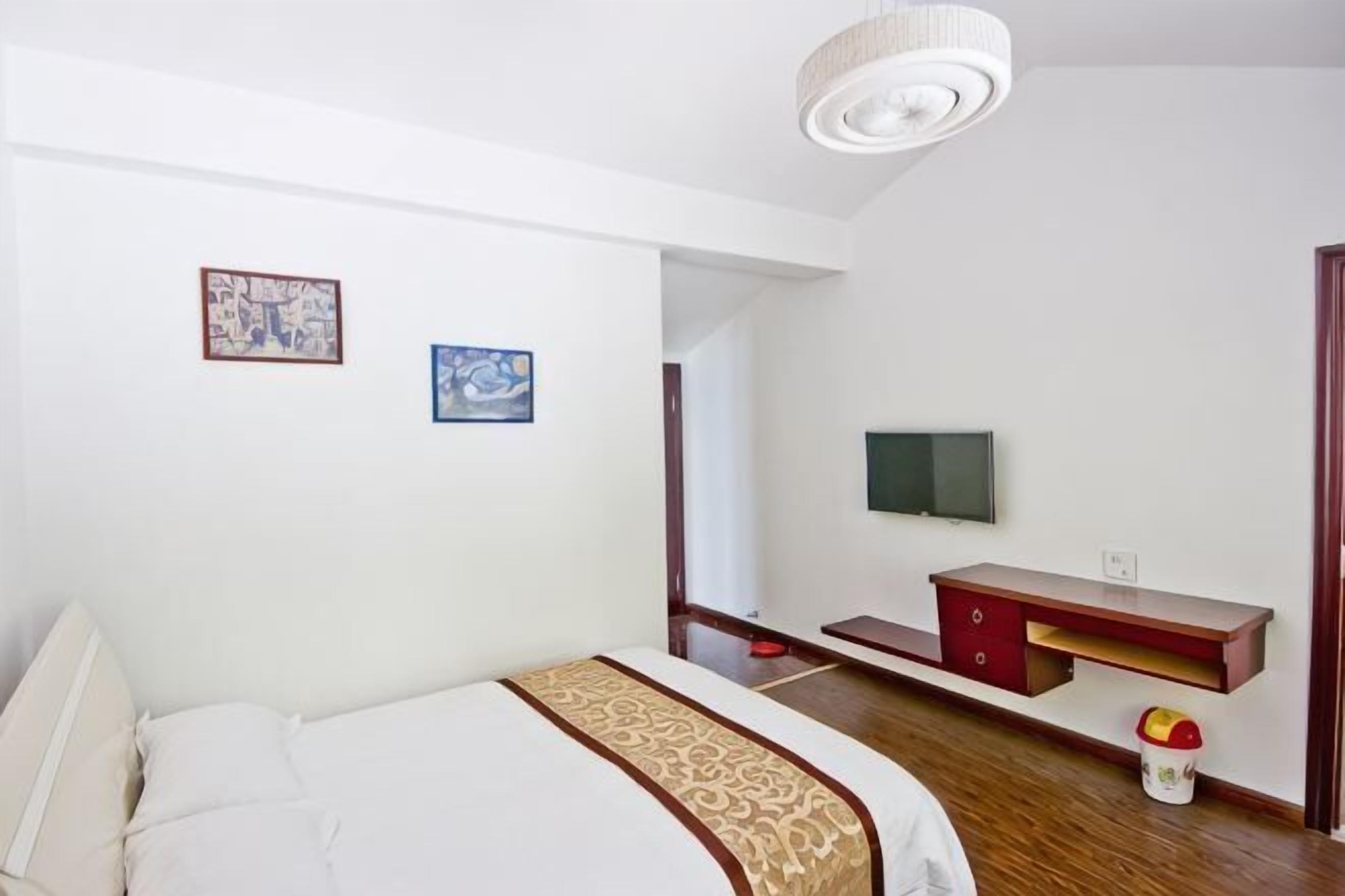 Quarto com cama, televisão, escrivaninha e uma pequena mesa com um vaso.