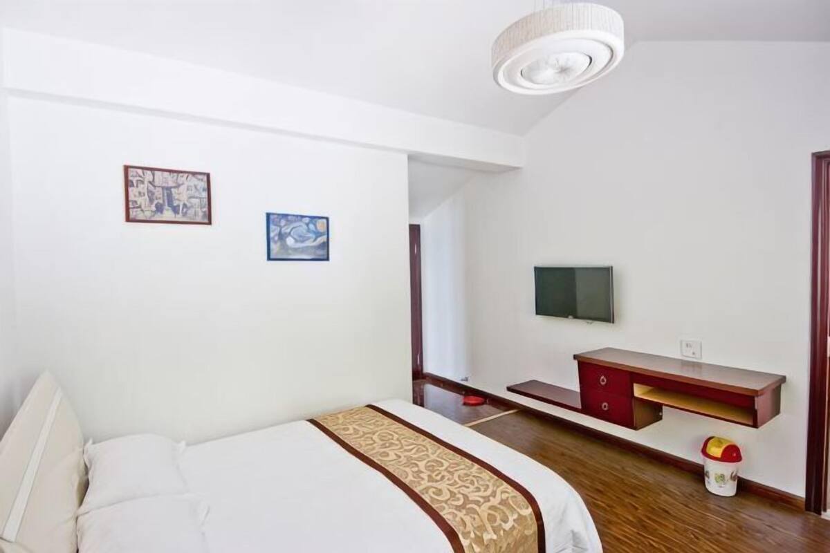 A bedroom with a bed, a TV, a desk, and a small table with a vase.