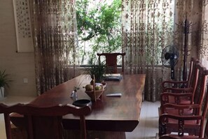 A dining area with a wooden table, chairs, a potted plant, and a fan. - Yandangshan Yunshuijian Homestay (Yueqing)