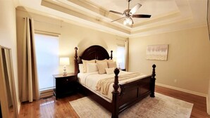 A bedroom with a wooden bed, a nightstand, a ceiling fan, and a large window with curtains. - Southern Belle (Clarksville)