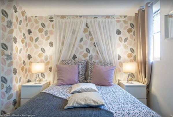 Une chambre à coucher avec un lit, deux tables de chevet, une commode et une fenêtre avec des rideaux.