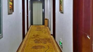 A hallway with a patterned carpet, doors on either side, and a light switch on the wall.