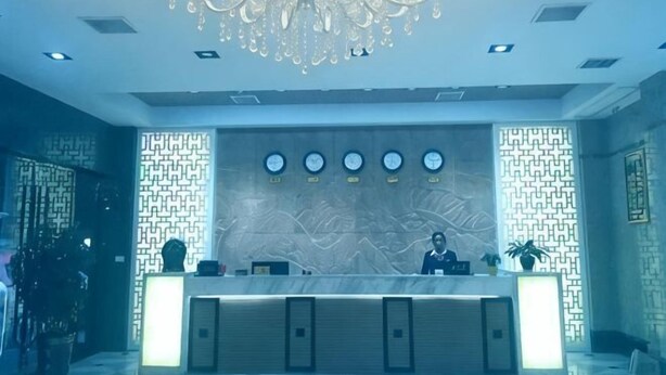 Zona de recepción de hotel con mostrador de mármol, candelabro y pared con diseño.