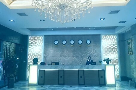 A hotel reception area with a marble counter, a chandelier, and a patterned wall.. Yuhuangge Hotel