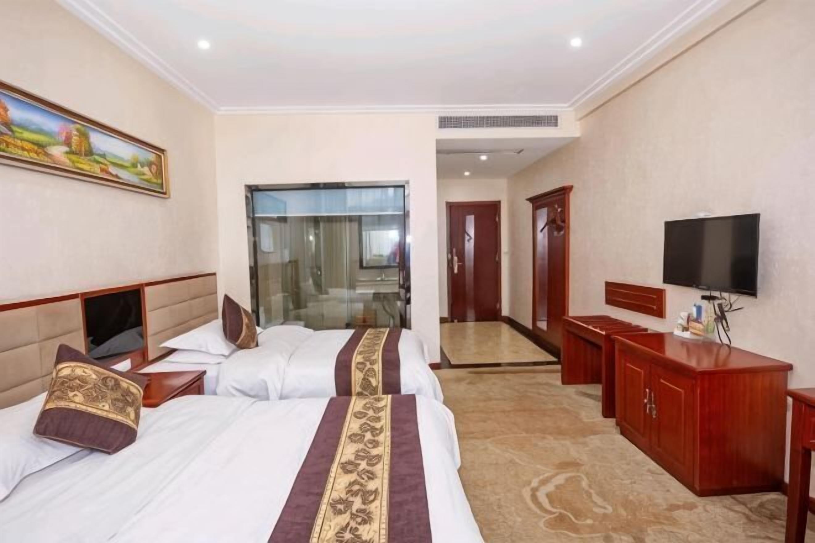 A hotel room with two beds, a TV, a desk, and a mirror.