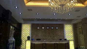 A hotel reception area with a marble counter, a chandelier, and patterned wall designs.