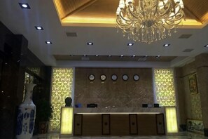 Zona de recepción de hotel con mostrador de mármol, una araña y diseños de pared estampados.