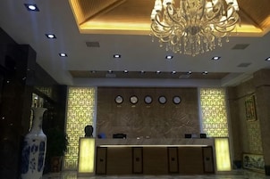 Zona de recepción de hotel con mostrador de mármol, una araña y diseños de pared estampados.