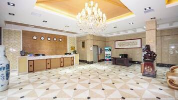 A hotel lobby with a reception desk, a chandelier, a large vase, and a statue.