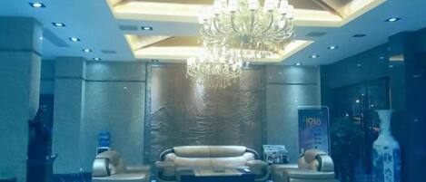 Um hall de entrada com um lustre, sofás, uma mesa de centro e um vaso decorativo.