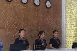 Receptionists seated at a counter with clocks on the wall behind them. - Yuhuangge Hotel (Badong)
