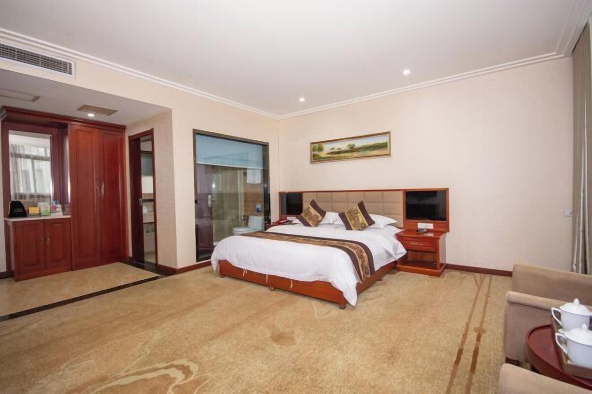 A hotel room with a large bed, a desk, a chair, and a painting on the wall.