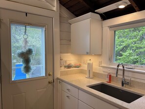 A kitchen with a sink, countertop, cabinets, and a window with a view of greenery.