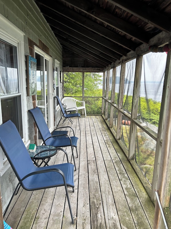 A covered porch with wooden flooring and metal chairs.
