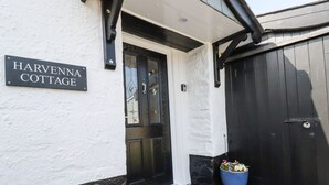 A cottage entrance with a black door, a sign reading "Harvenna Cottage", and a blue flower pot on the steps.