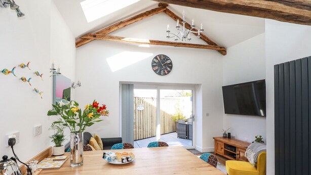 A modern kitchen with a wooden island, a dining area with a yellow chair, and a TV mounted on the wall.