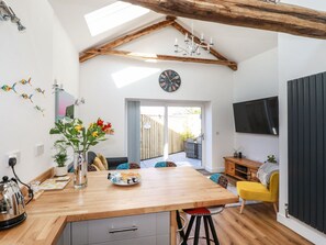 Une cuisine moderne avec un îlot central en bois, un coin repas avec une chaise jaune et un téléviseur fixé au mur.