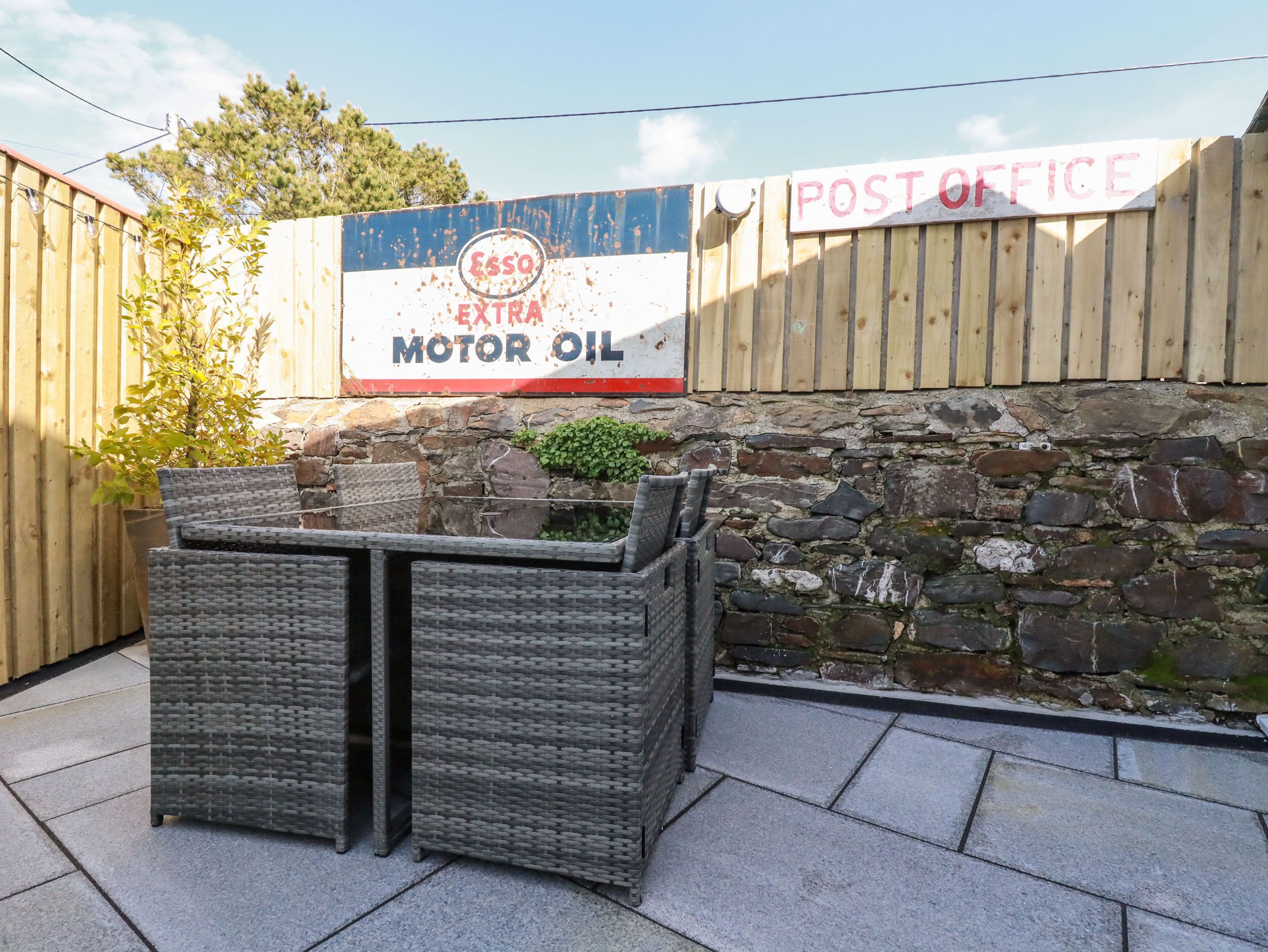A patio area with wicker furniture, a stone wall, and a sign for ESSO EXTRA MOTOR OIL.