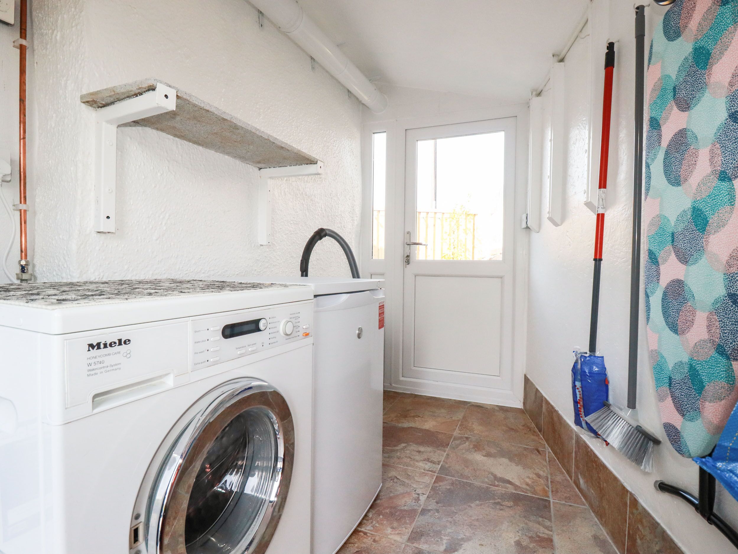 Une buanderie équipée d’un lave-linge Miele à chargement frontal, d’un étendoir et d’une porte donnant sur l’extérieur.