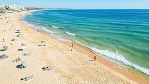 A beach with people sunbathing, umbrellas, and a clear blue sea.
