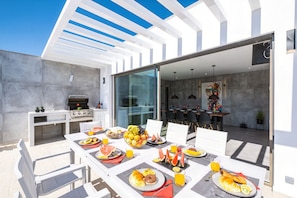 An outdoor dining area with a grill, breakfast foods, and a view into the house.