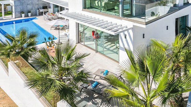 A modern multi-story house with a glass-enclosed balcony, a swimming pool, and outdoor furniture.