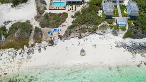 Luchtbeeld van een landgoed aan de kust, met een groot huis, een zwembad en een strand.