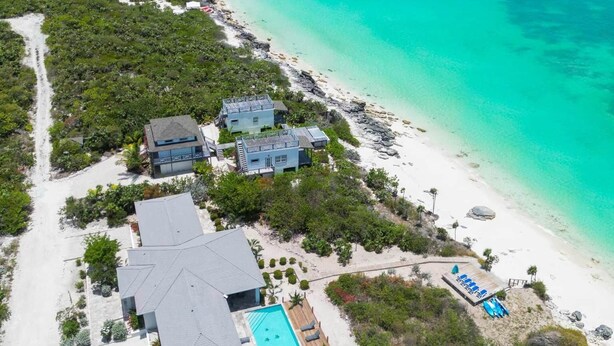 Luchtbeeld van een kustresort met zwembad, toegang tot het strand en helder turquoise water.