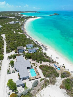 An aerial view of a coastal resort with a swimming pool, beach access, and clear turquoise waters. - Blue Reef Villa, big patio, snorkelling reef & on a swimmable lazy river! (Moore Hill)
