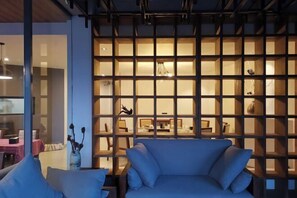 Een moderne zithoek met een blauwe bank, een houten scheidingswand met verlichte planken, en een eethoek op de achtergrond.