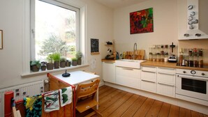 A kitchen with white cabinets, a wooden countertop, and a window with potted plants. - Family Friendly Funhouse Centrally Located in Ottensen (Hamburg)