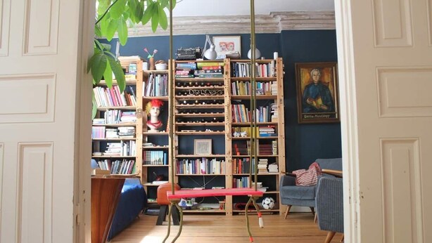 A cozy living room with a bookshelf, a red bench, a blue sofa, and a soccer ball on the floor. - Family Friendly Funhouse Centrally Located in Ottensen (Hamburg)