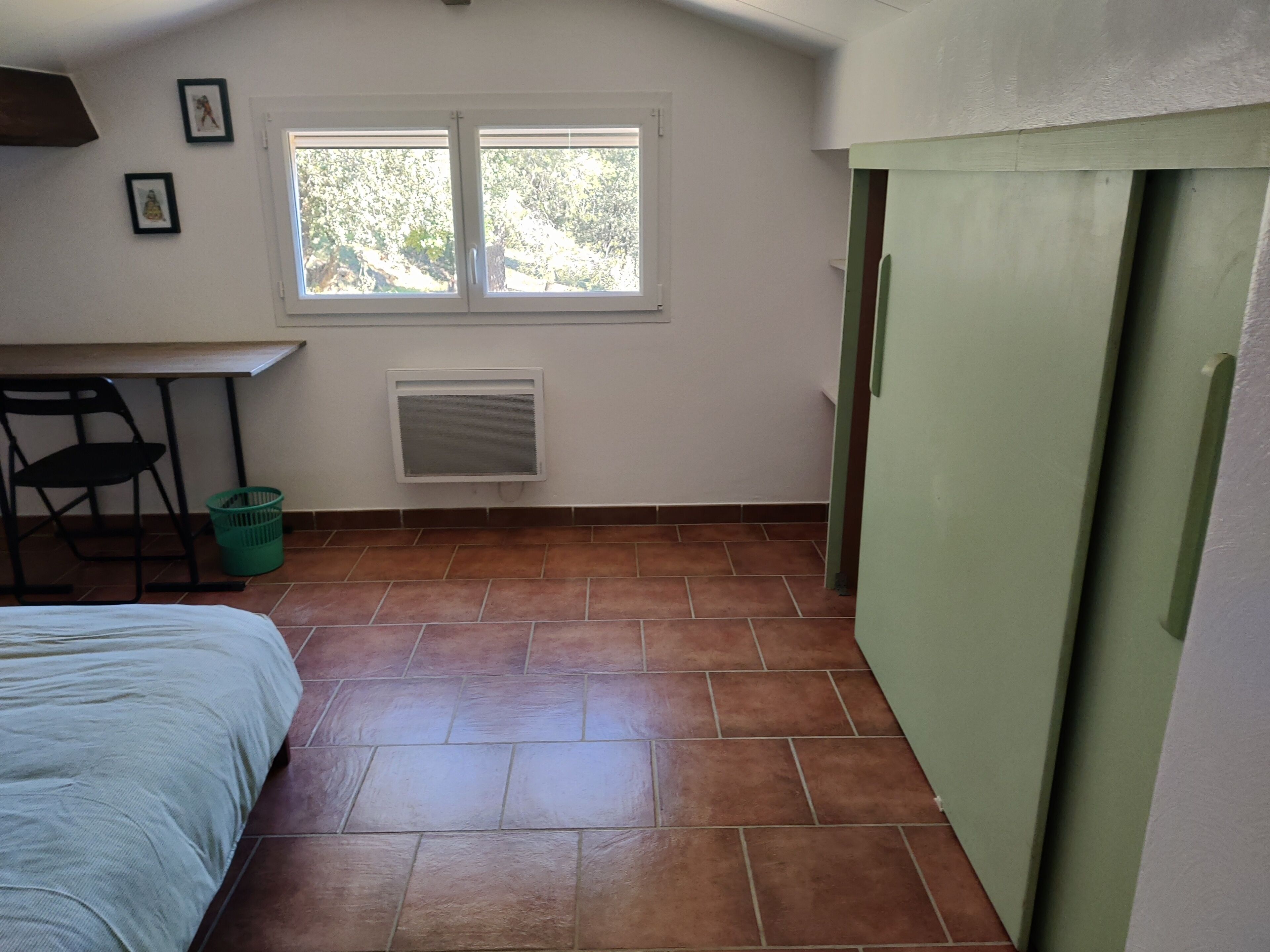 A small room with a bed, a desk, a chair, a window, and a radiator.