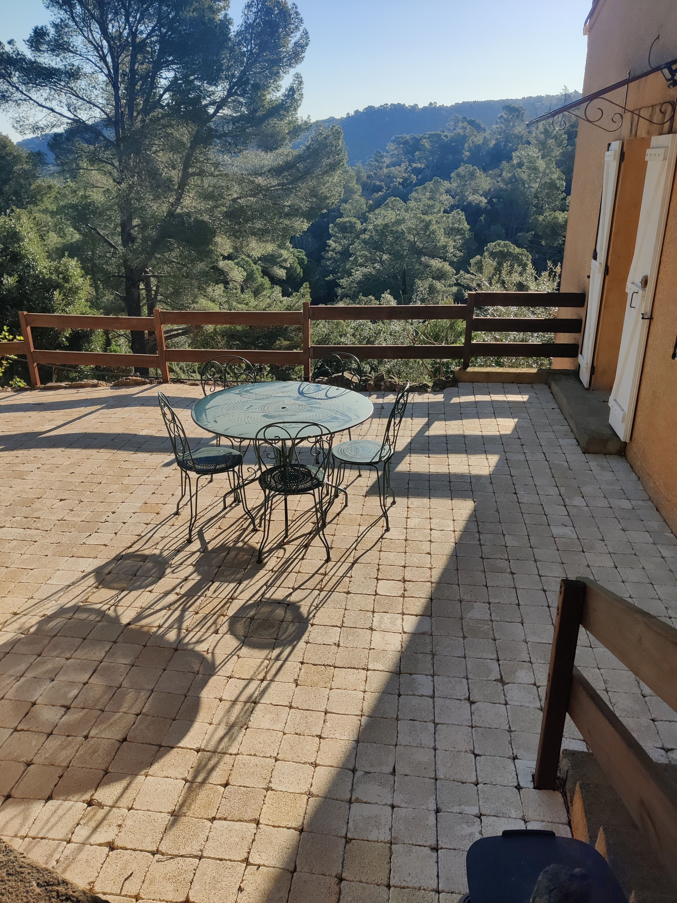 A patio with a round table and chairs, a wooden fence, and a view of a forested hillside.