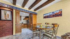 Un comedor con una mesa redonda y sillas, una cocina al fondo y un cuadro de un paisaje montañoso en la pared.