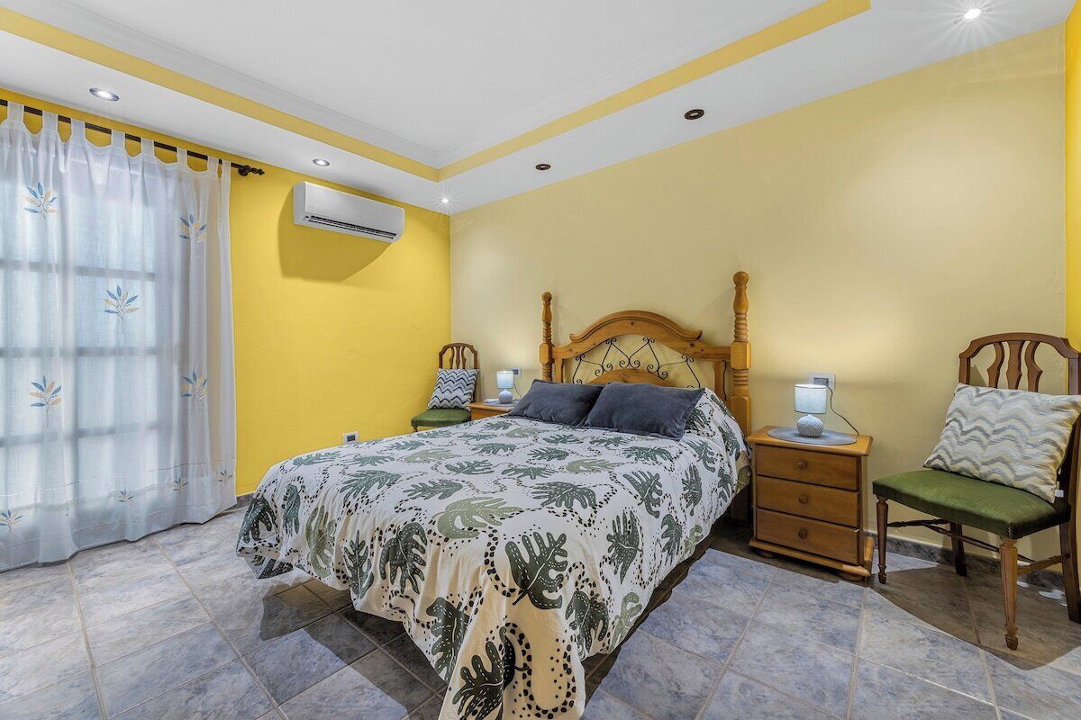 A bedroom with a bed, bedside tables, a chair, and an air conditioning unit.