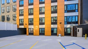 A modern building with a distinctive orange and white facade, large windows, and a parking area with marked spaces. - Sleep Inn Bronx - Soundview (Bronx)