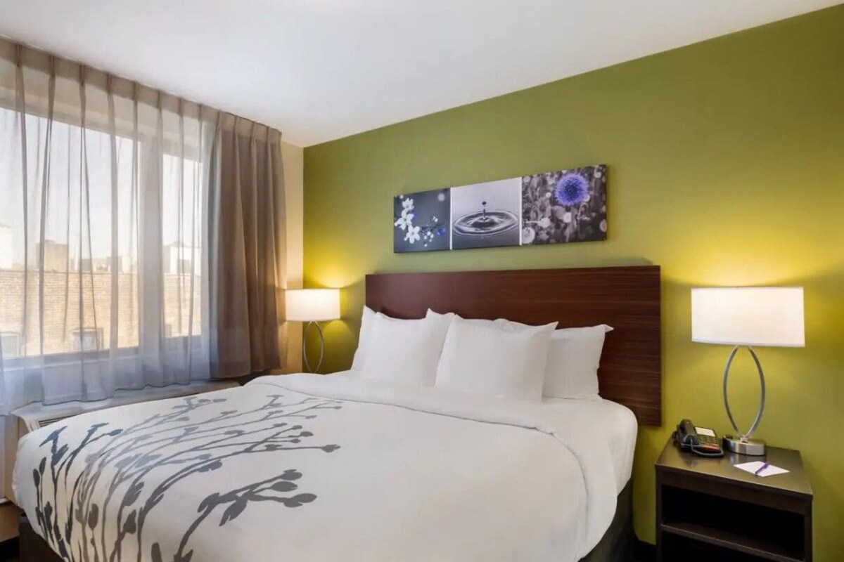 A hotel room with a large bed, two bedside lamps, a nightstand, and a wall-mounted artwork.