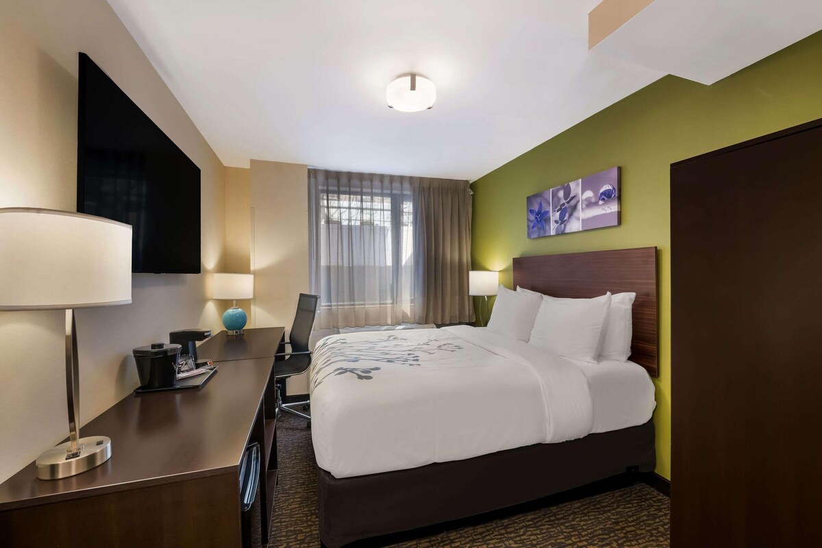 A hotel room with a bed, desk, chair, lamp, and a window with curtains.