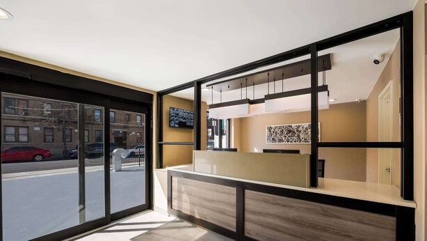A modern reception area with a glass door leading to a street view, a reception desk, and a mounted television. - Sleep Inn Bronx - Soundview (Bronx)