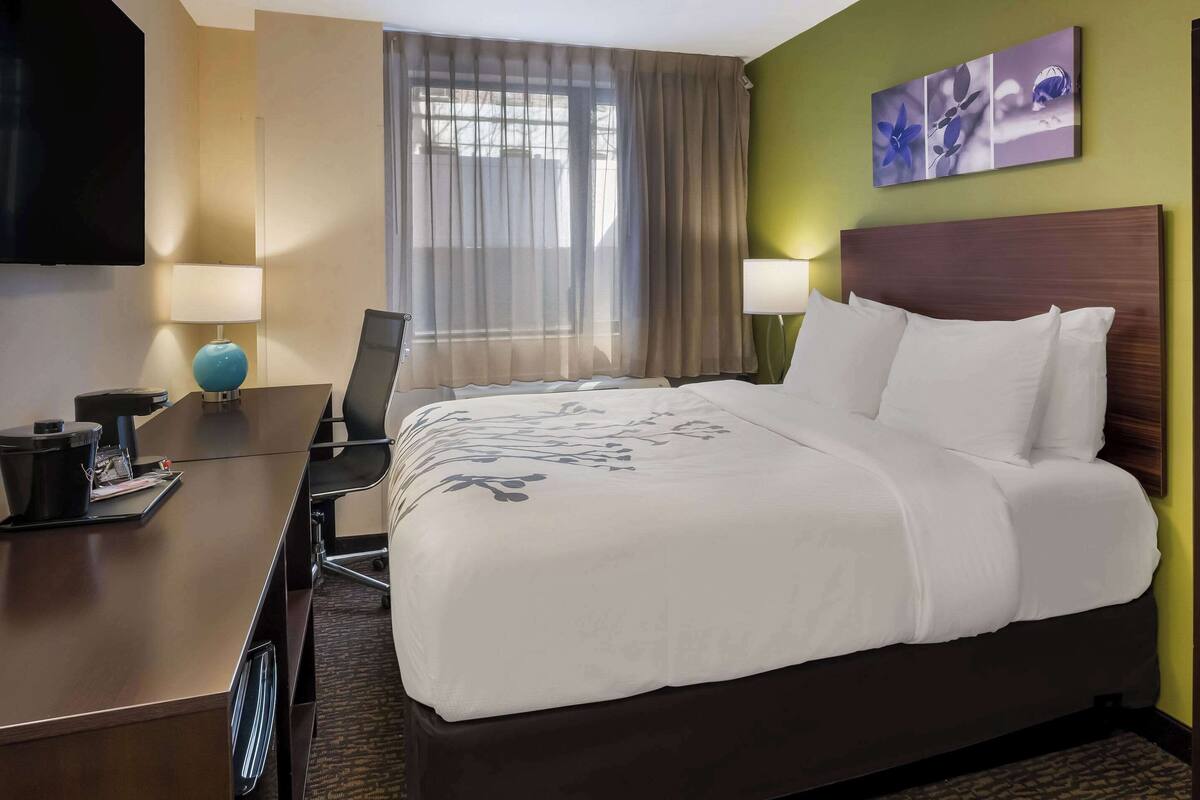 A hotel room with a bed, a desk, a chair, a TV, and a window with curtains.