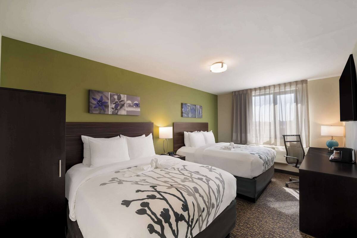 A hotel room with two beds, a desk, a chair, and artwork on the walls.